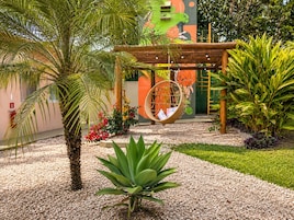 Un jardín con una silla colgante, palmeras y un mural.