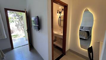 Un bagno con specchio, lavabo e doccia. C'è una TV a parete e una porta che dà su una zona esterna.