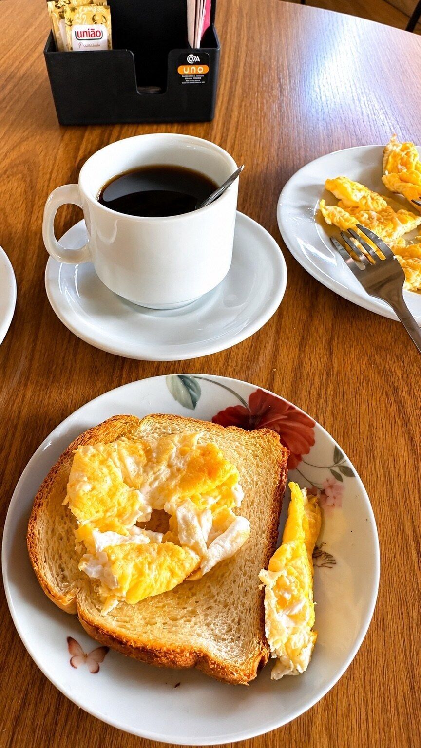 Een ontbijttafel met een kop koffie, roerei op toast en een bord roerei.