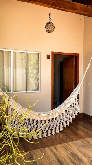 A room with a hammock, wooden flooring, a window with curtains, and a door.