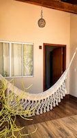 Una habitación con una hamaca, piso de madera, una ventana con cortinas y una puerta.