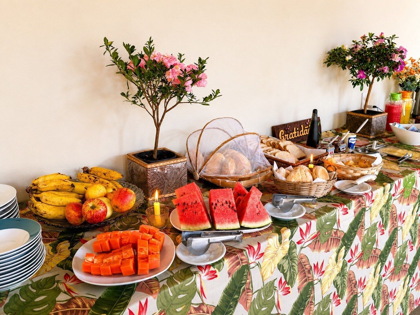 Uma mesa de buffet com diversas frutas, pães e uma pequena planta em vaso.