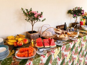 A buffet table with various fruits, bread, and a small potted plant.