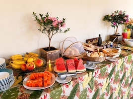 Una mesa de buffet con diversas frutas, pan y una pequeña planta en maceta.