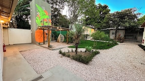 A courtyard with a mural, a small palm tree, and a gravel path.