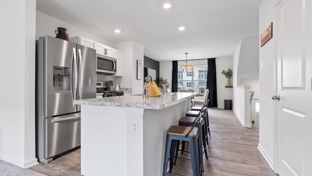 A modern kitchen with a stainless steel refrigerator, microwave, and island with bar stools. - Elegant New Home Near Lakes - Relax & Unwind! (Bull Valley)