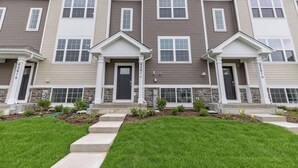 A row of townhouses with a uniform design, featuring a central entrance with a door and windows on each side. - Elegant New Home Near Lakes - Relax & Unwind! (Bull Valley)