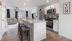A modern kitchen with white cabinets, stainless steel appliances, and a central island with bar stools. - Elegant New Home Near Lakes - Relax & Unwind! (Bull Valley)