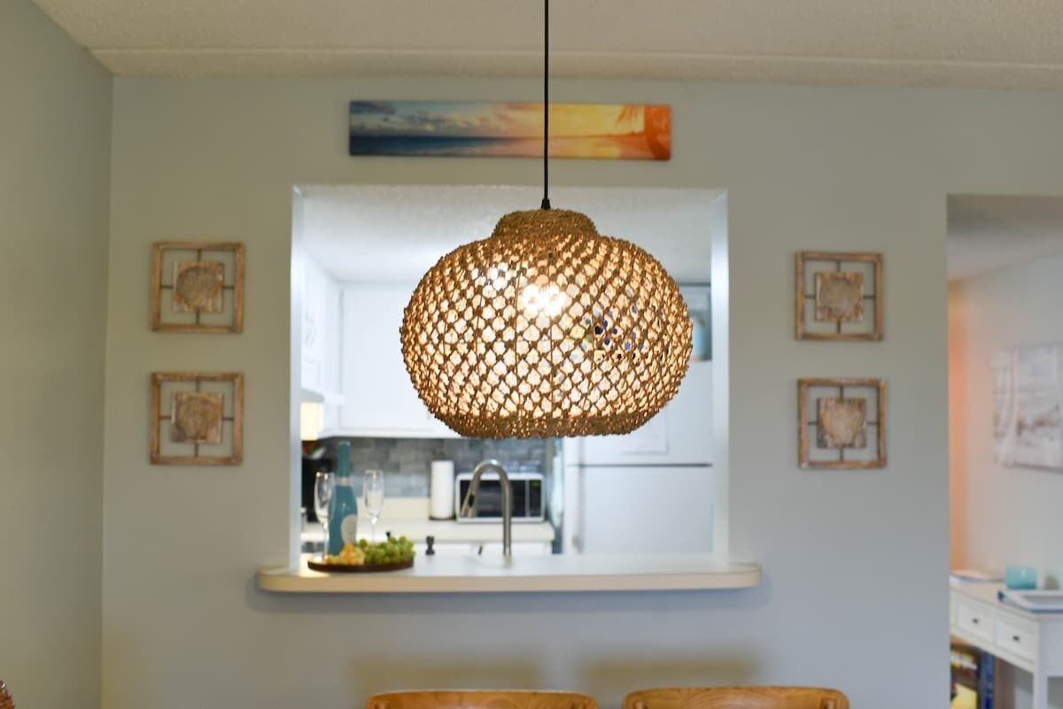 En matplats med en rund, flätad taklampa som hänger från taket, en vit bänkskiva med en diskho och inramade konstverk på väggarna.