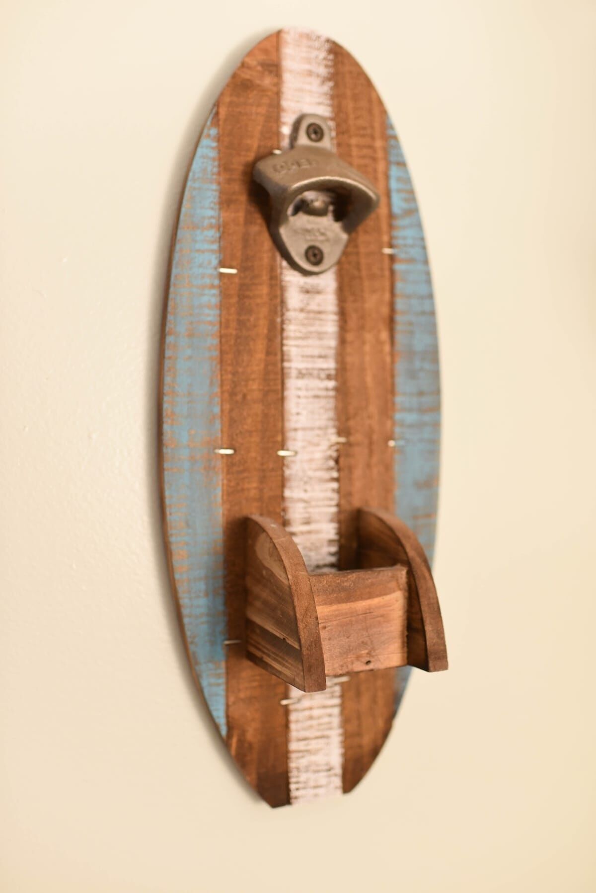 A wooden surfboard wall-mounted with a metal bottle opener.