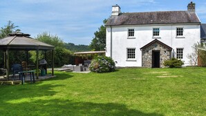 Une maison blanche avec une entrée en pierre, un patio couvert avec des meubles d’extérieur et une pelouse bien entretenue.