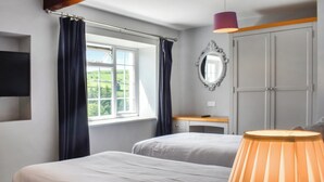 Une chambre avec deux lits, une fenêtre avec des rideaux, un miroir, une armoire et une lampe.