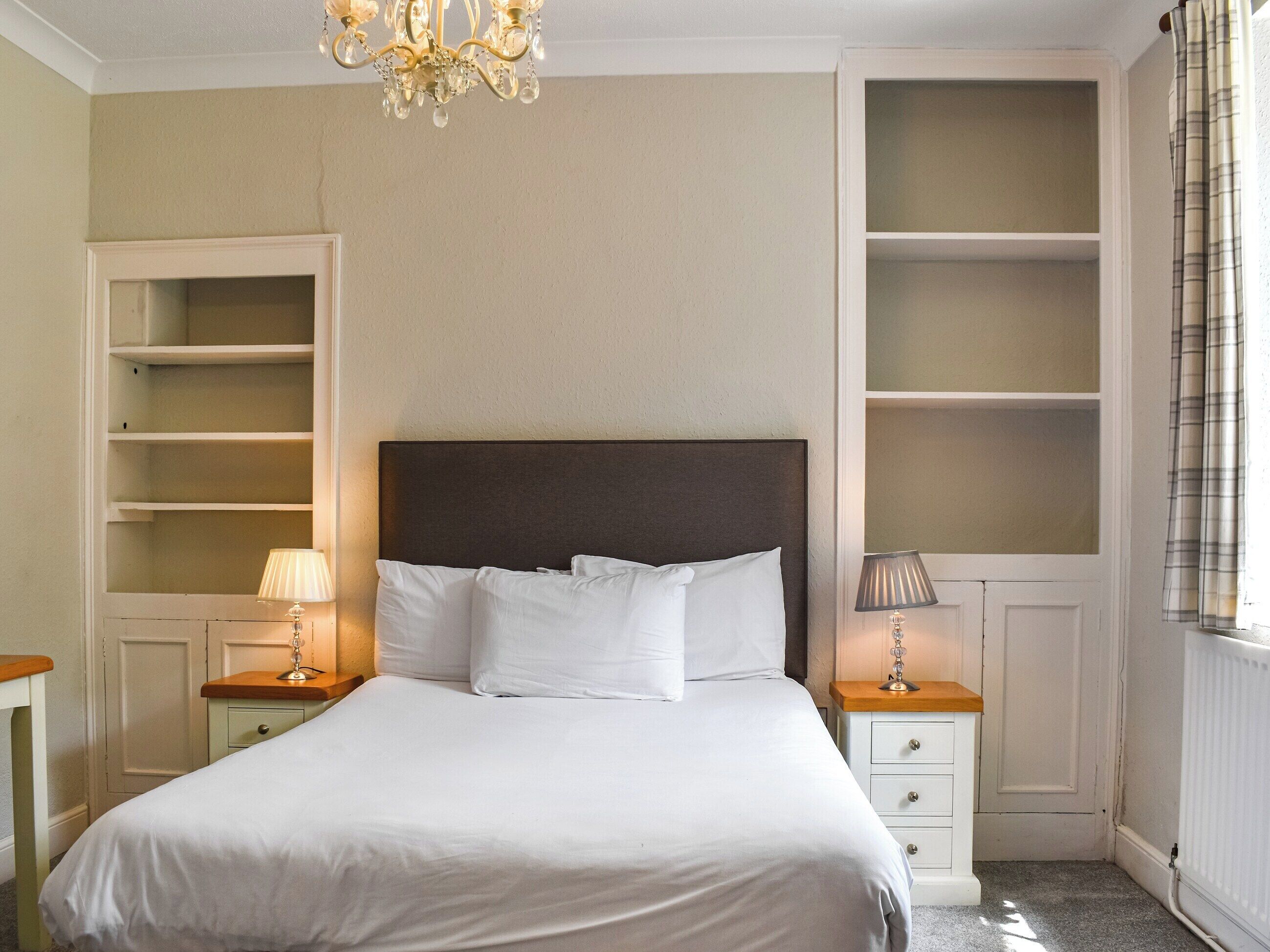 Una camera da letto con un letto grande, due comodini con lampade, un lampadario e scaffali a muro.