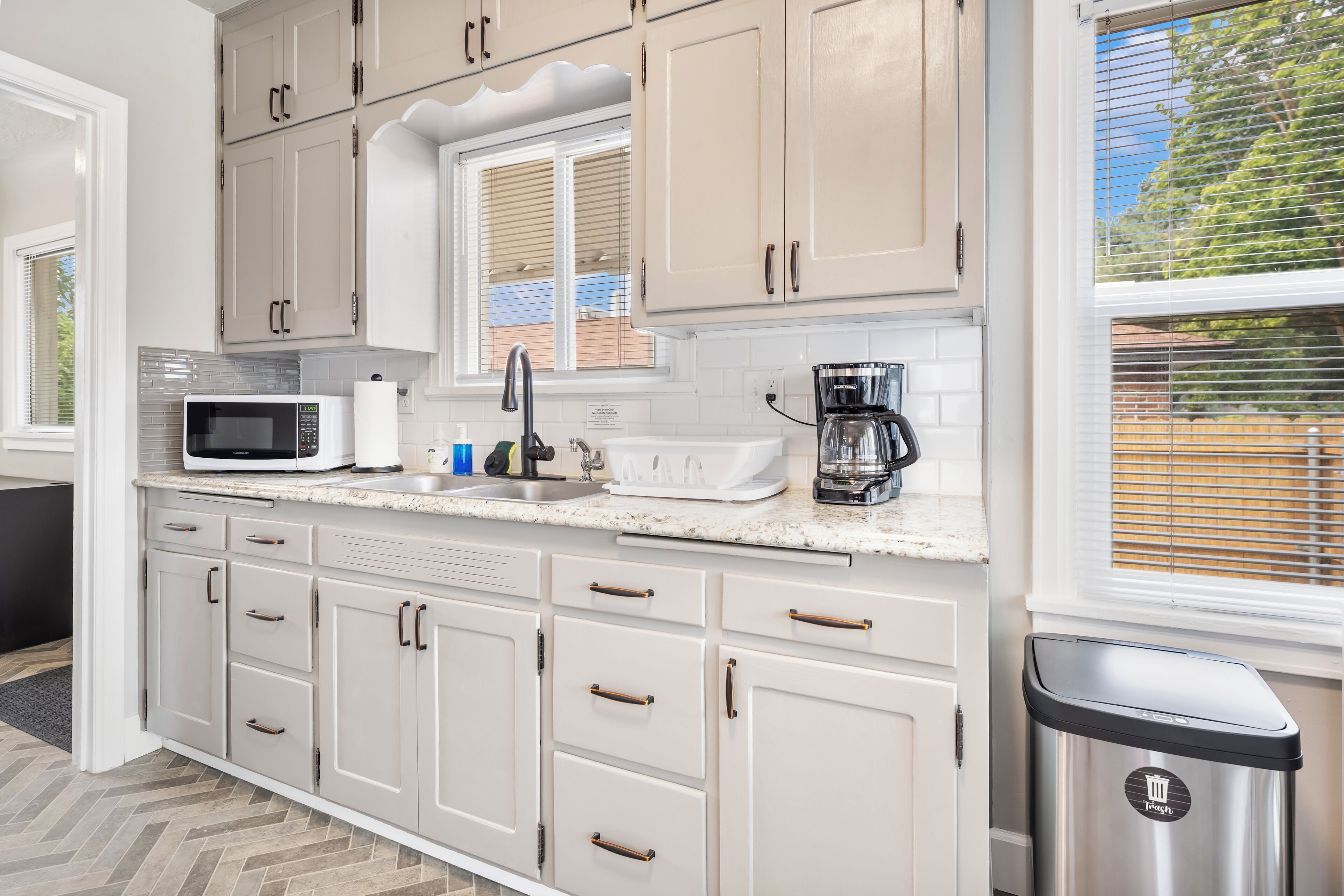 A kitchen with white cabinets, a microwave, a coffee maker, and a trash can.