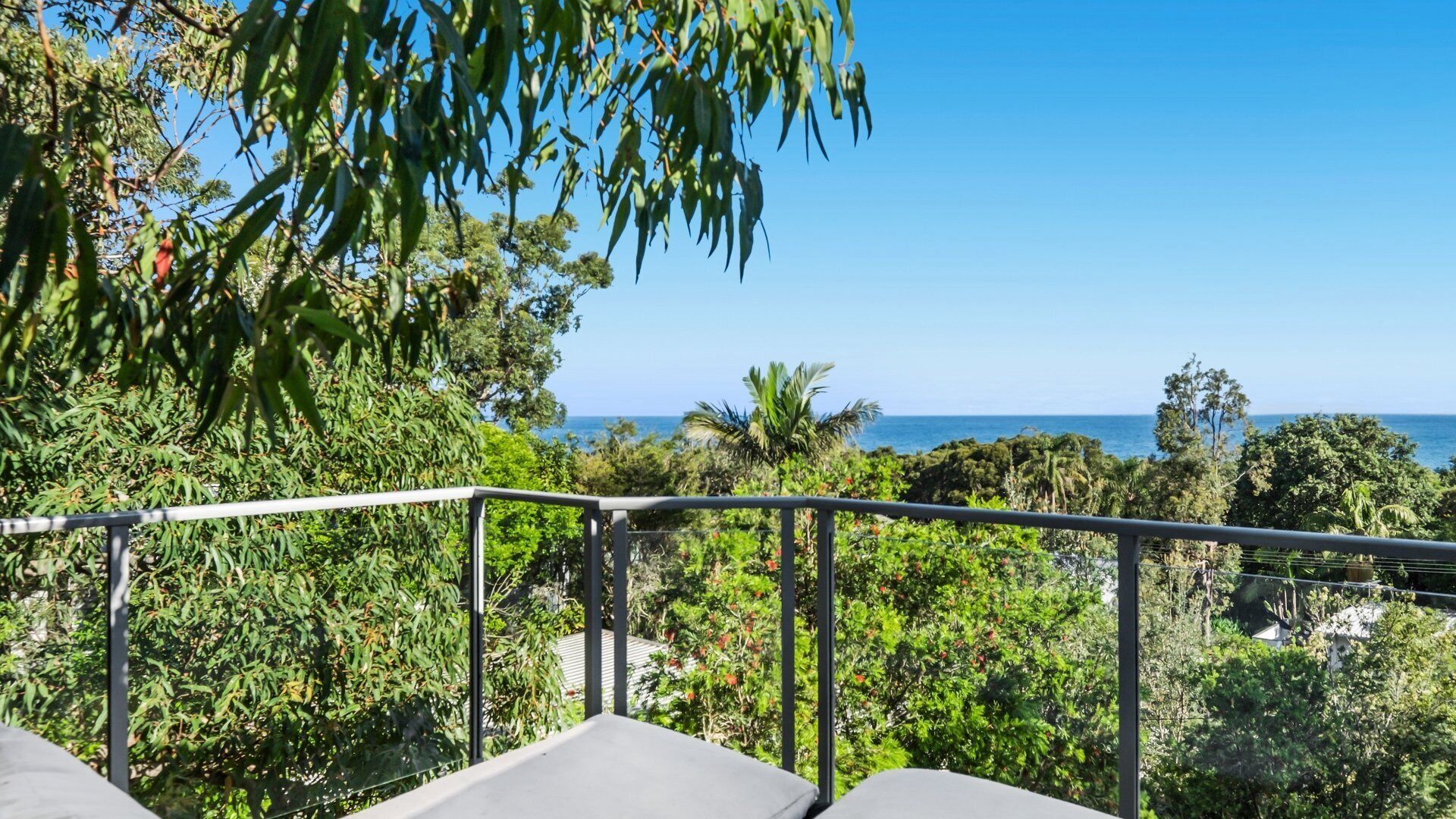 A balcony with a view of the ocean, surrounded by lush greenery.