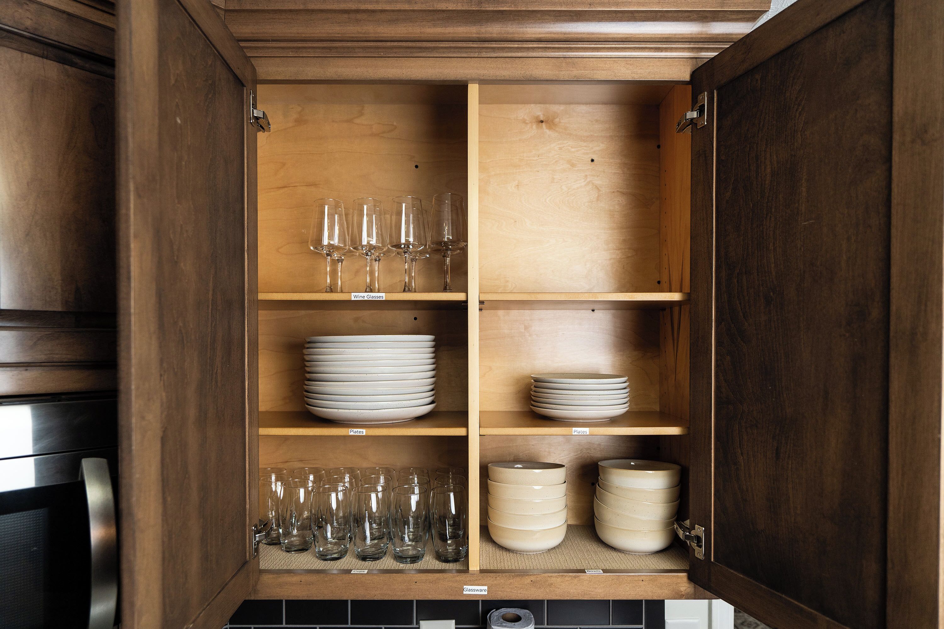 Un mueble de madera con estantes que contienen copas de vino, platos y cuencos.