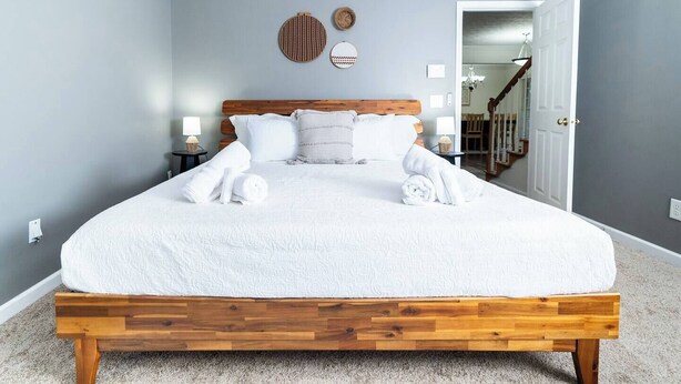 Un lit bien fait, avec du linge de lit blanc et des serviettes pliées, une tête de lit en bois et deux tables de chevet avec des lampes.