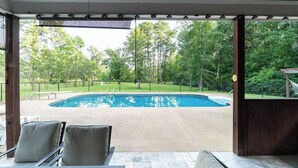 Un espace extérieur abrité comprenant une piscine, des chaises et une vue sur une zone boisée.
