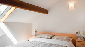 Un dormitorio con techo inclinado, una cama con edredón a cuadros, una mesita de noche con lámpara y un tocador con lámpara.