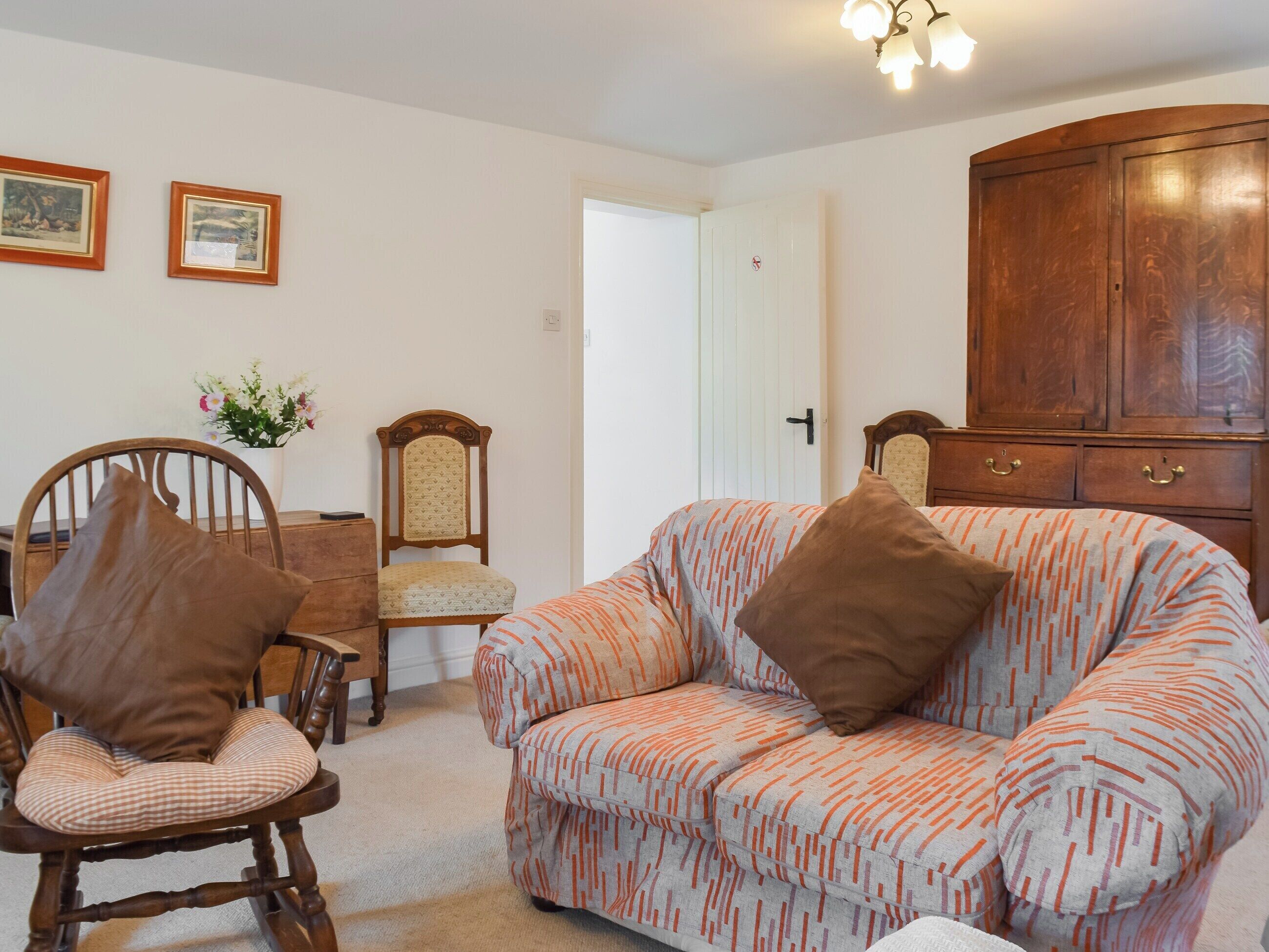 Una sala de estar con un sofá, un sillón mecedora, un aparador de madera y una mesa de comedor con sillas.