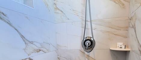 A bathroom with marble walls, a shower with a rain showerhead, and a mosaic floor.