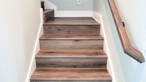 Un escalier avec des marches en bois et une rampe, menant à un mur bleu clair orné d’une peinture abstraite aux couleurs vives.