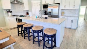 Une cuisine moderne avec des meubles blancs, un réfrigérateur en acier inoxydable et un îlot central doté de tabourets de bar.
