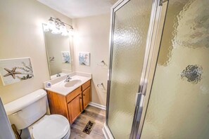 Un baño con inodoro, lavamanos, tocador y ducha con puerta de cristal.