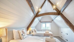 Une chambre avec deux lits, une fenêtre et un plafond en pente avec des poutres apparentes.