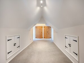 Un couloir étroit avec un plafond en pente, des portes en bois et un sol recouvert de moquette.