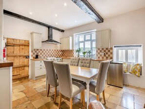 Een keuken met een eettafel, stoelen, een fornuis en een raam.