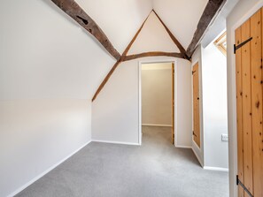 Ein Zimmer mit geneigter Decke, freiliegenden Holzbalken, Teppichboden und einer Holztür.