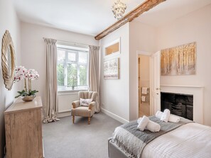 Een slaapkamer met een open haard, een raam met gordijnen, een stoel, een bed met handdoeken en een spiegel.