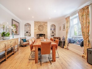 Una sala da pranzo con tavolo e sedie in legno, un camino, scaffali con oggetti decorativi e una finestra con tende.