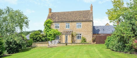 A two-story stone house with a well-maintained lawn and a small patio area.