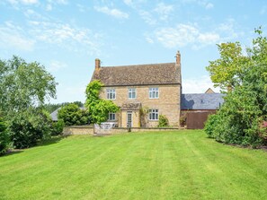 A two-story stone house with a well-maintained lawn and a small patio area.