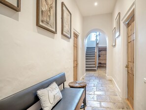 Un corridoio con una panca, opere d'arte incorniciate, porte in legno e una scala.
