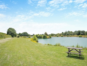 Une table de pique-nique au bord d’un lac, avec des berges verdoyantes et des arbres en arrière-plan.