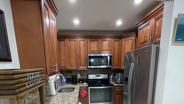A kitchen with wooden cabinets, a stainless steel refrigerator, a microwave, an oven, and a granite countertop.