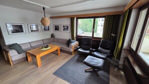 A modern living room with a sofa, a coffee table, a black leather chair, a wooden table, and a hanging light fixture.