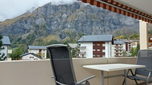 A balcony with a table and chairs, overlooking a mountain and residential buildings.