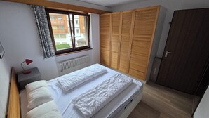 A bedroom with a bed, a window, a radiator, a wardrobe, and a door.