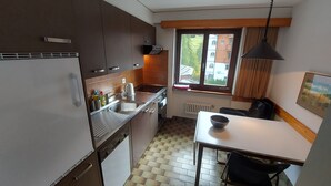 A compact kitchen with a window, a dining table, and a black chair.