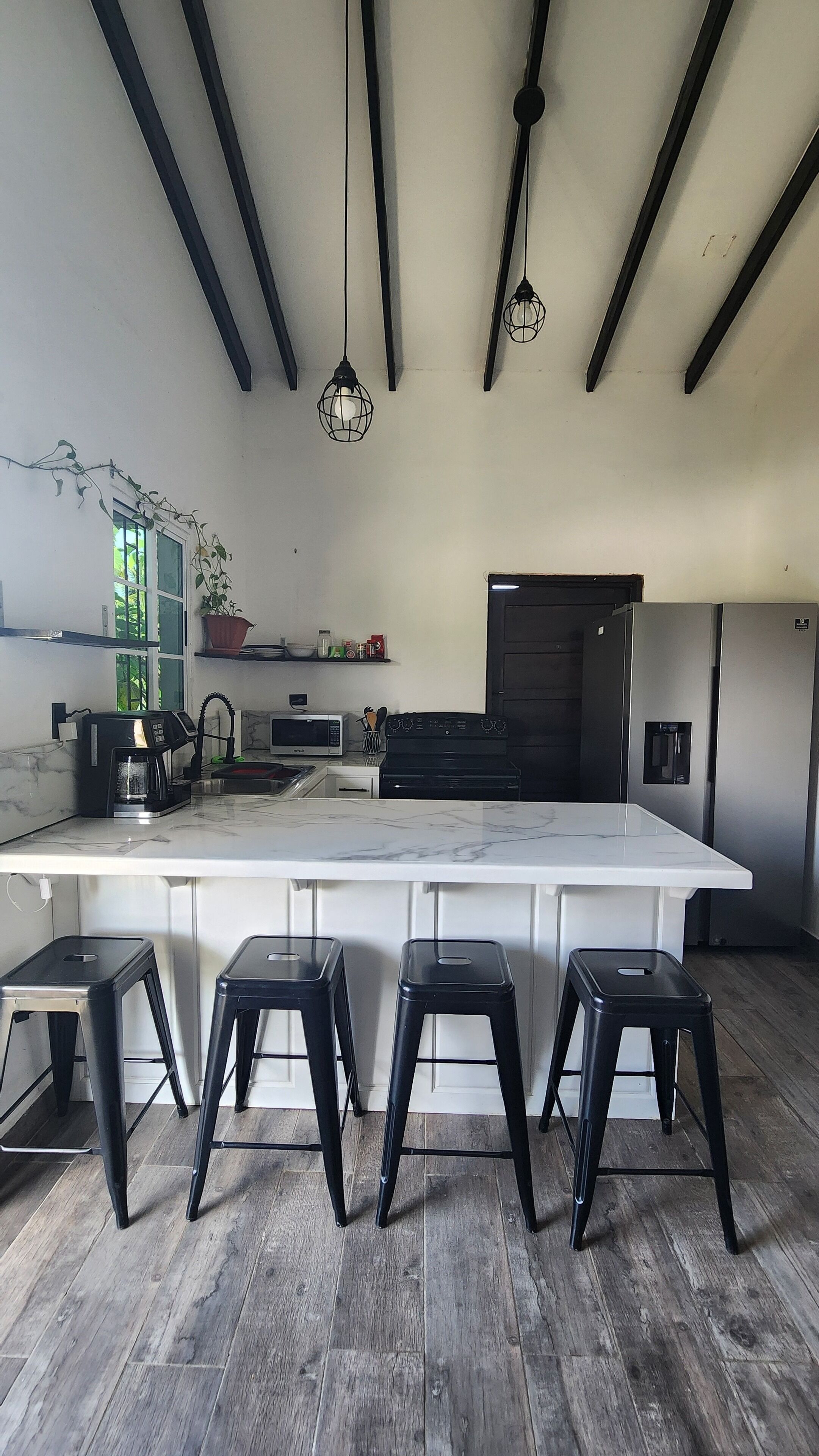 A modern kitchen with a large island, black stools, a microwave, a coffee maker, and a refrigerator.