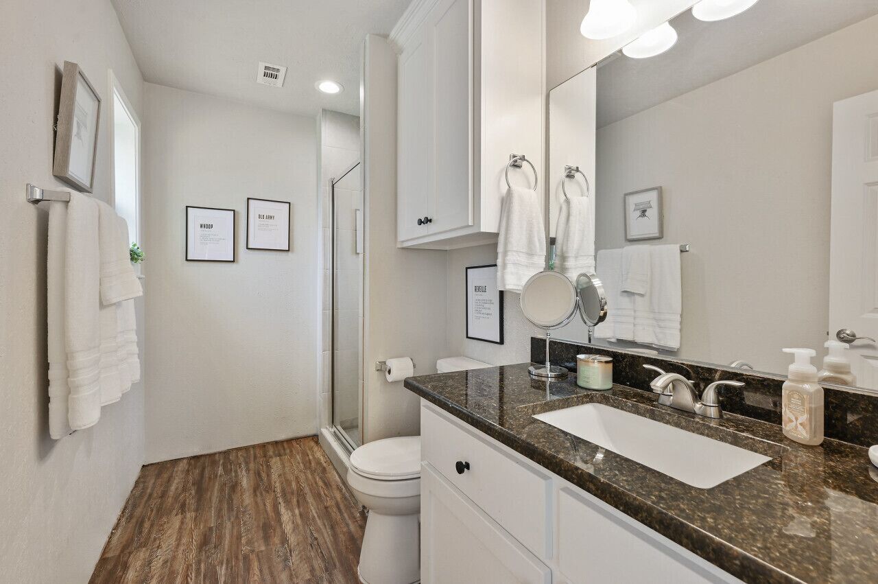 A modern bathroom with a shower, toilet, and sink. There are framed pictures on the wall and a large mirror above the sink.