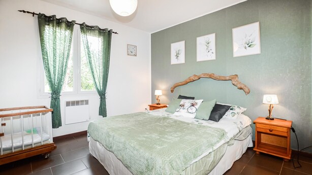 Ein Schlafzimmer mit einem großen Bett, einem Babybett, grünen Vorhängen und Wandbildern.