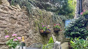 A stone wall with hanging flower baskets, a metal table with chairs, and potted plants. - 3 bedroom accommodation in Bakewell (Bakewell)