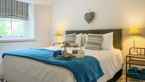 A neatly made bed with a blue blanket, a heart-shaped wall decoration, and two bedside lamps. - 3 bedroom accommodation in Bakewell (Bakewell)