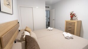 A hotel room with a bed, a wooden dresser, and a framed picture on the wall. - 097 - Club Náutico 012 - comfortHOLIDAYS (Santa Pola)