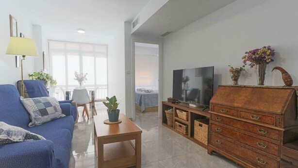 A living room with a blue sofa, a wooden coffee table, a TV stand, and a cabinet. - 097 - Club Náutico 012 - comfortHOLIDAYS (Santa Pola)